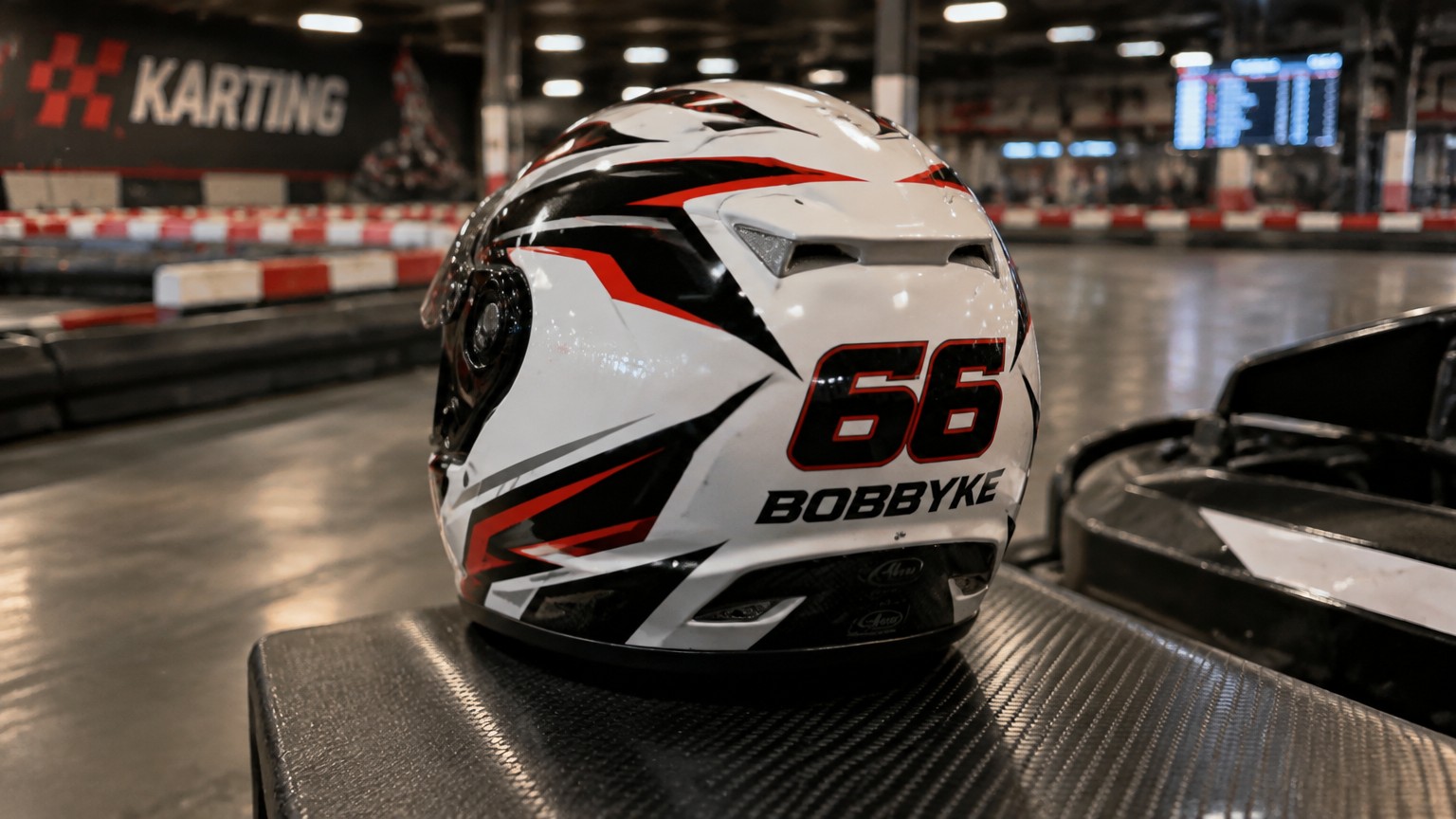 maak een helm op een indoor karting baan en maak de helm met als basis kleur wit met zwarte rode en grijze lijnen en zet op de achterkant een numme 66 met de naam bobbyke er bij
